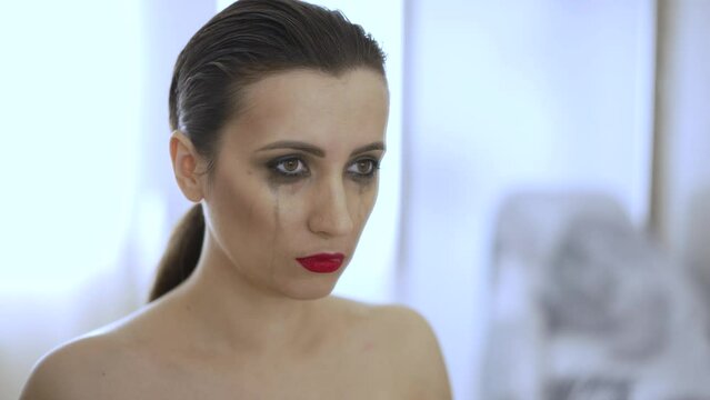 Woman with smeared mascara looks at the mirror