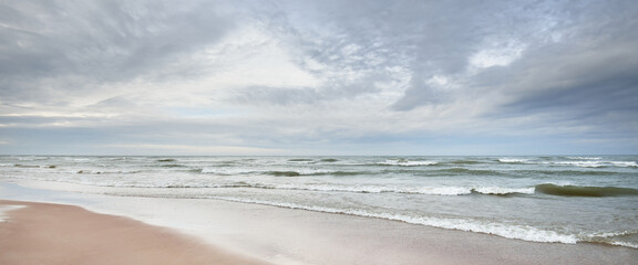 Panoramic view of the Baltic sea from a sandy shore (sand dunes). Dramatic sky with glowing clouds,...