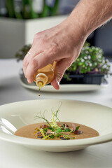 The process of decorating the mushroom cream soup. Chef puts spices and mushrooms on a plate