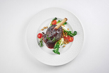 Slow cooked lamb Shank in wine sauce on a white plate on a white tablecloth