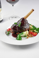 Slow cooked lamb Shank in wine sauce on a white plate on a white tablecloth