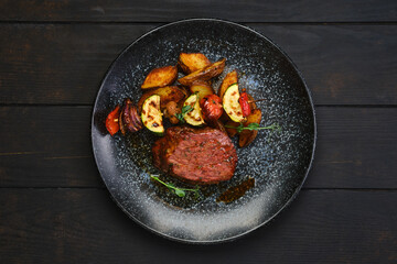 Overhead view of beef steak with potato wedges and grilled vegetables