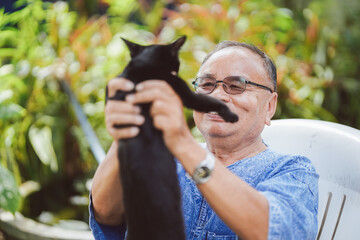 Senior man and black cat playing in the garden of the house. Concept of mental health care.