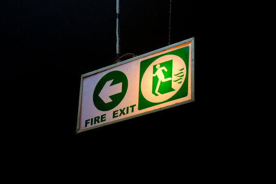 Fire Exit Sign Hanging From A Ceiling Isolated On A Black Background