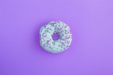 Donut with blue glaze on the purple background. Copy space. Close-up.