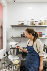 Female pastry chef using an electric mixer while cooking in the bakery kitchen.