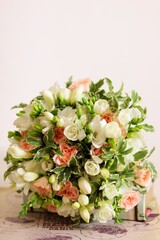 Round Bouquet of white freesia flower, pink roses and leaves and book on light beige background.  Bunch of flowers, vintage style, top view, vertical photo.