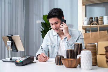 Asian young man talk with customer on phone to check vase goods order. 