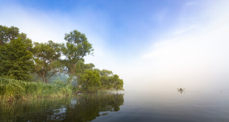 Mystical landscape. Fog in the early morning on the river. The trees near the water are illuminated by the rays of the rising sun.