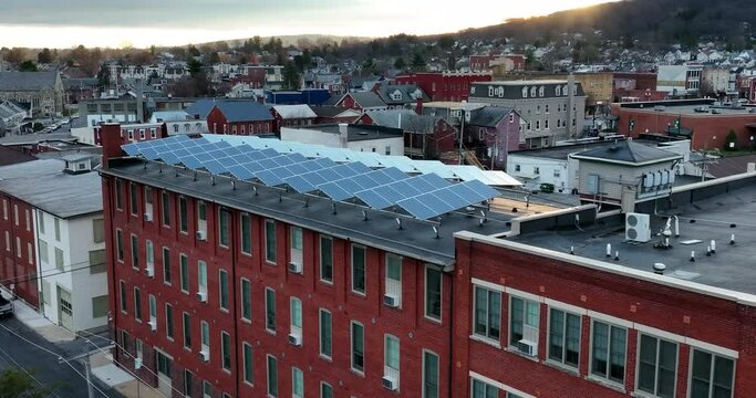 Solar panel arrays collect sunlight for green renewable energy at apartment building. Aerial tilt up reveals sun and sunrise in small town America.