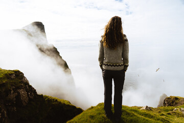 Naklejka premium woman on a cliff in front of the ocean on a foggy day