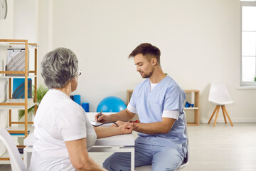 Fototapeta premium Doctor checking blood pressure of his senior patient with hypertension. Mature lady getting her arterial pressure measured while sitting at desk during her checkup visit to modern clinic or hospital