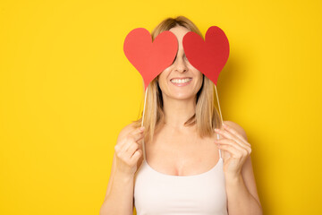 Portrait of smiling young woman holding paper hearts, posing and looking at camera isolated on yellow background. Love And Valentines Day Concept.