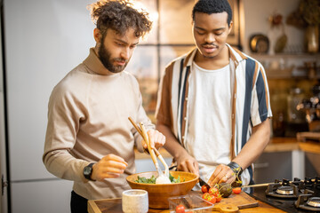 Two guys of different ethnicity cooking healthy vegan food on kitchen at home. Concept of close male friendship or relationship as gay. Idea of healthy eating