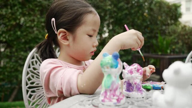 Adorable Asian girl kid toddler having concentrate with stucco doll painting at the backyard house. Child development small muscle by doing artwork.