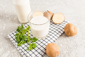 a glass of vegetable milk from potato tubers on a cloth towel and a gray concrete background with potato tubers and a bottle of milk.