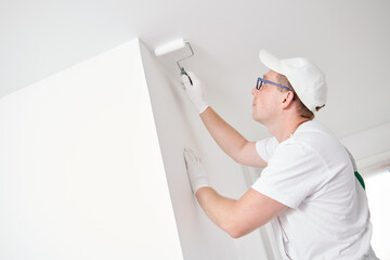 Painter worker with roller painting ceiling surface into white