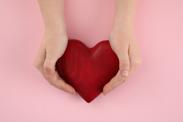 Woman holding red heart on pink background, top view