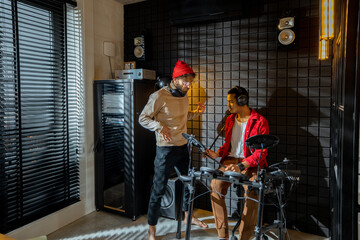 Two stylish men playing electric drums at small recording studio. Interior view on home studio....