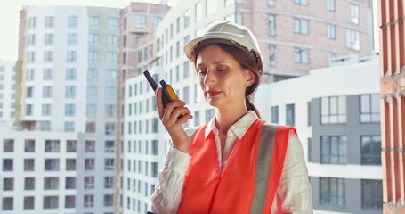 Builder in helmet talking by walkie talkie control and communicate with worker outdoors on construction site at village. Contractor using radio operation in industry.