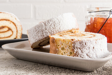 two pieces of tender apple roll on a ceramic plate against a white brick wall and a jar of jam. delicious dessert. Snack.