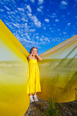Fototapeta na wymiar Ukrainian patriot girl in a yellow dress against a blue sky. Summer photo. Blue sky. Sunny day. Free Ukrainian child. Child symbol of Ukraine