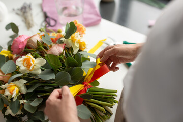 people, gardening and floral design concept - close up of woman or floral artist making bunch of flowers and tying bow on table at studio