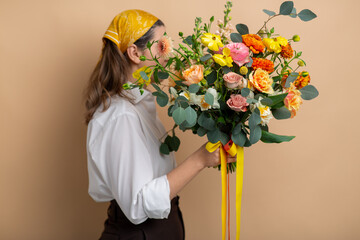 people and floral design concept - woman holding bunch of flowers over beige background