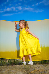 Obraz premium Ukrainian girl 7 years old, she is a patriot of Ukraine, dressed in a yellow dress against a blue sky. Blue sky. Sunny day. Free Ukrainian child. Child symbol of Ukraine