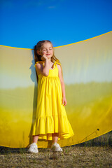 Obraz premium Ukrainian girl 7 years old, she is a patriot of Ukraine, dressed in a yellow dress against a blue sky. Blue sky. Sunny day. Free Ukrainian child. Child symbol of Ukraine