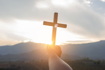 Human hand praying and holding a Christian cross for worship.