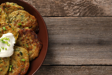 Delicious zucchini pancakes with sour cream and green onion on wooden table, top view. Space for text
