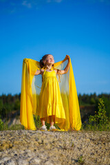 Naklejka premium The symbol of freedom is a Ukrainian girl of 7 years old, patriotically dressed in a yellow dress against a blue sky. Blue sky. Sunny day. Free Ukrainian child. Child symbol of Ukraine