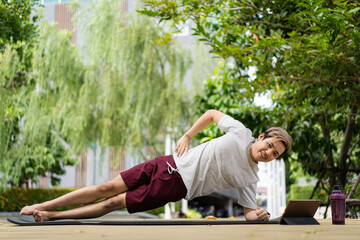 Active sportsman doing a side plank exercise and making a video call with a friend and online sport training coach. 