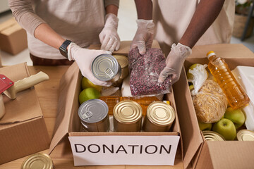 High angle shot of unrecognizable man and woman wearing protective gloves packing food supplies into cardboard boxes for charity