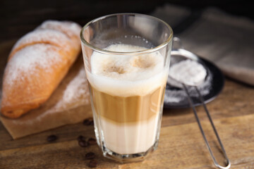 Delicious latte macchiato, croissant and scattered coffee beans on wooden table