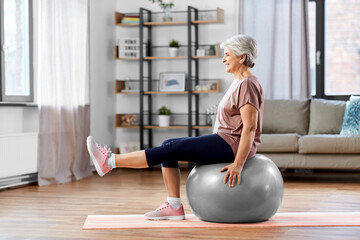 sport, fitness and healthy lifestyle concept - smiling senior woman training by sitting on exercise...