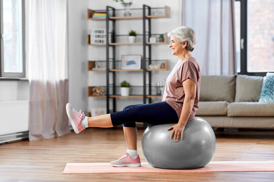 sport, fitness and healthy lifestyle concept - smiling senior woman training by sitting on exercise ball at home