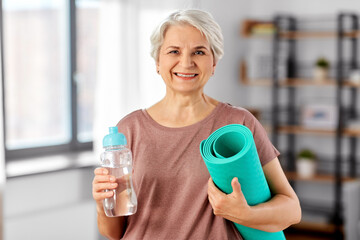 sport, fitness and healthy lifestyle concept - smiling senior woman with yoga mat and bottle of...