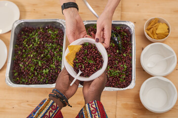 Top-down shot of unrecognizable volunteer giving bowl with nutritious lunch meal to poor African person in modern charity organization