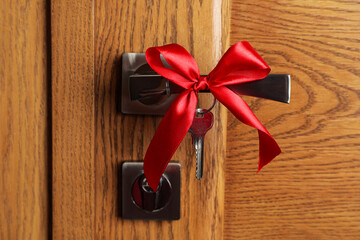 Key with red bow on door handle, closeup view. Housewarming party