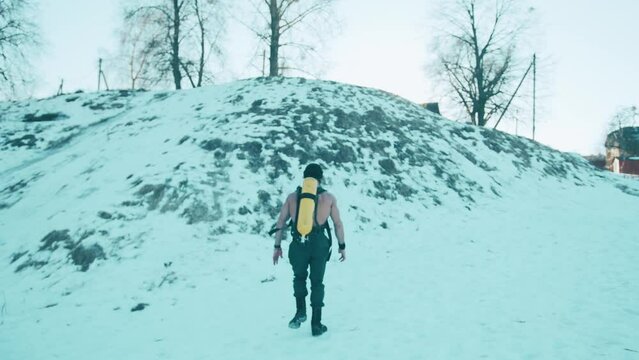 Muscular man with a naked torso with a ballon compressed air drager on his back and full face mask climbs a snowy hill
