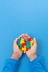 World autism awareness day concept. Child hand holding colorful puzzle heart on light blue background