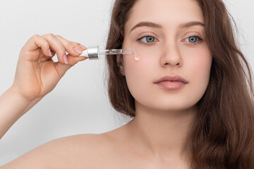 Fototapeta premium Young woman applying serum to her face, looking away.