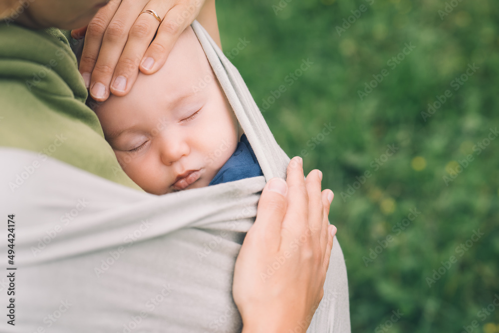 Wall mural Babywearing. Mother and baby on nature outdoors. Baby in wrap carrier. Woman carrying little child in baby sling in green mint color. Concept of green parenting, natural motherhood, postpartum period.