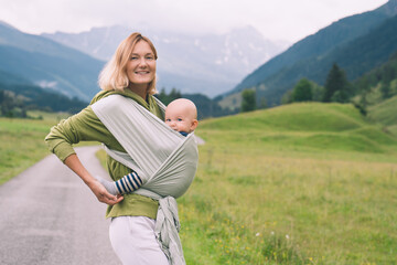 Naklejka na ściany i meble Babywearing. Mother and baby on nature outdoors. Baby in wrap carrier. Woman carrying little child in baby sling in green mint color. Concept of green parenting, natural motherhood, postpartum period.