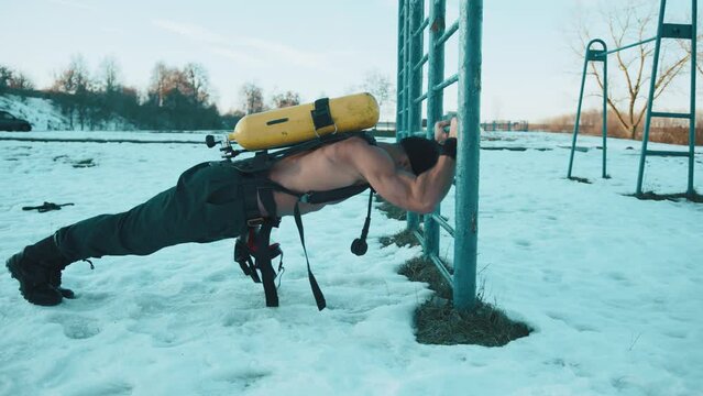Bodybuilder with a naked torso doing push-ups from the bar in the cold with a drager on his back and pumping the latissimus dorsi