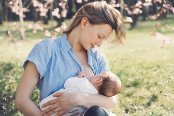Beautiful mother breastfeeding baby. Young woman breast feeding her newborn baby. Concept of lactation infant, postpartum period, natural motherhood. Mother and baby on nature outdoors. - obrazy, fototapety, plakaty