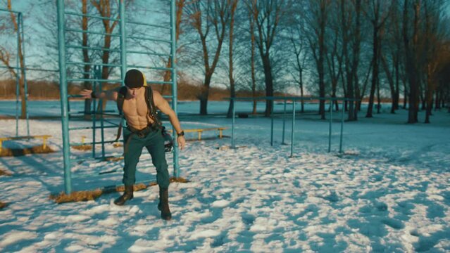 Young muscular man training in a winter park and doing a resistance exercise with a powerlifting band and with a compressed air bottle Drager