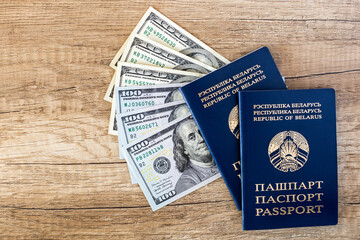 Two Belarusian passports on a brown wooden background with a fan of American dollars. Travel, help and immigration concept